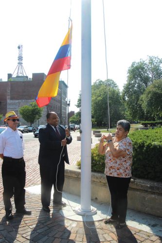 ➥➥ El Alcalde de Lawrence iza la bandera colombiana con la ayuda de Luz Echeverry en el Parque Campagnone el pasado 20 de julio.