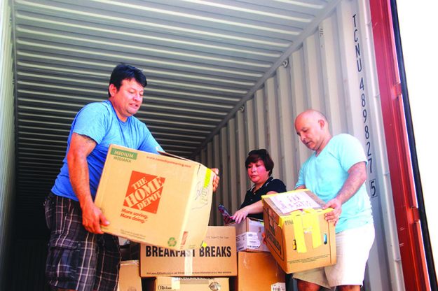 ➥➥ Angel Fernández a la izquierda y Luis Yépez acomodan las cajas en el contenedor con la ayuda de Alexandra Serrano. Foto por Yadira Betances.