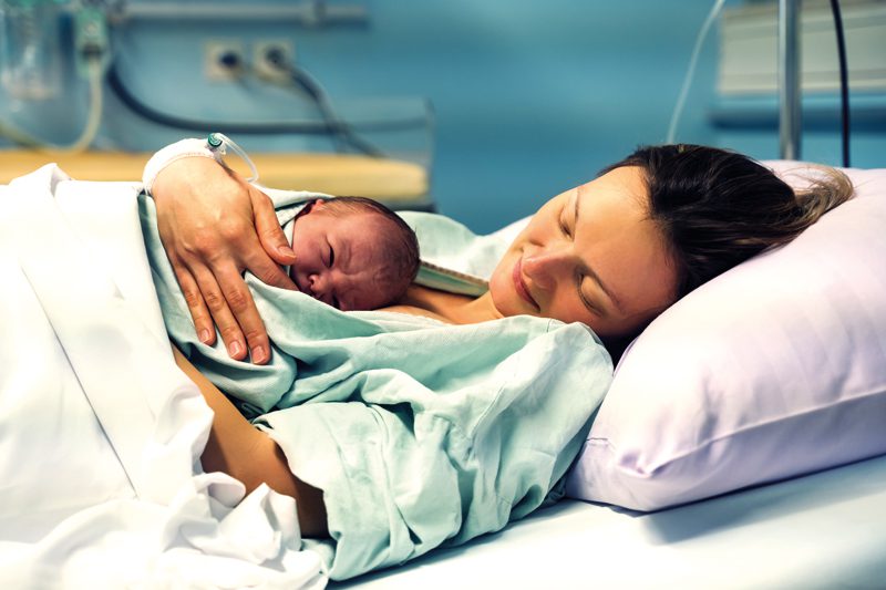 Mother and newborn. Child birth in maternity hospital. Young mom hugging her newborn baby after delivery. Woman giving birth. First moments of baby life after labor.