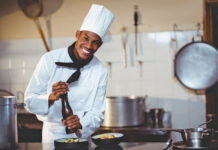 ¡Premios Buen Provecho! Portrait of chef sprinkling pepper on a meal in commercial kitchen