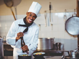 ¡Premios Buen Provecho! Portrait of chef sprinkling pepper on a meal in commercial kitchen